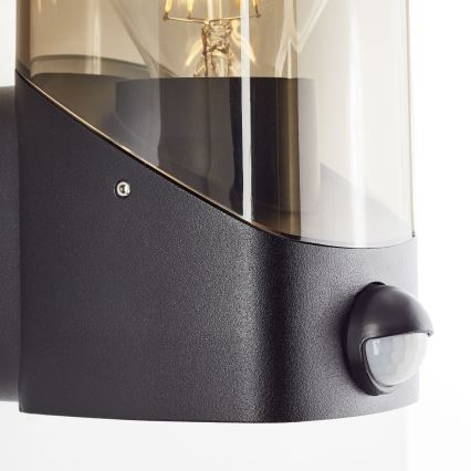 Brilliant - Φωτιστικό τοίχου εξωτερικού χώρου με αισθητήρα MINOU 1xE27/10W/230V IP44 μαύρο/φιμέ